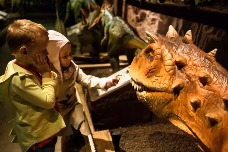 Zwei Kinder bestaunen einen realistischen Dinosaurier im Tirolland – ein interaktives Erlebnis für spannende Indoor Aktivitäten in Tirol.