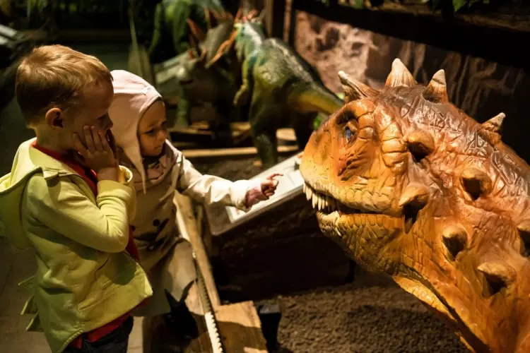 Zwei Kinder entdecken fasziniert einen Dinosaurier in der interaktiven Ausstellung im Tirolland – ein unvergessliches Erlebnis beim Ausflug in Tirol.