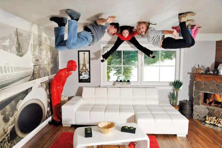 Drei Personen hängen scheinbar kopfüber in einem Wohnzimmer – eine verblüffende Illusion im Tirolland, die einen Ausflug in Tirol unvergesslich macht.