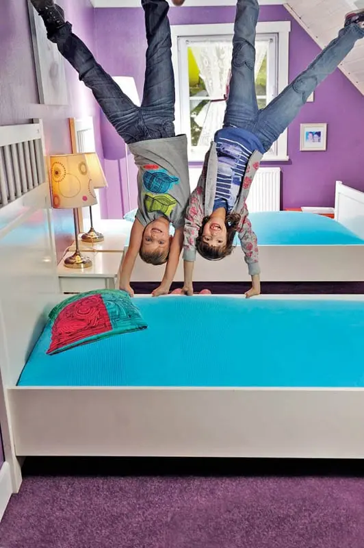 Zwei Kinder hängen kopfüber in einem Schlafzimmer im Tirolland – eine lustige Illusion beim Ausflug in Tirol.
